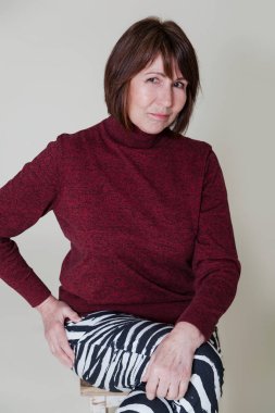 Basit ışık arka plan üzerinde oturan yaşlı kadın portresi. Emeklilik yaşı iyi durumda kadın yaramazca kameraya gülümsüyor ve iyi bir ruh hali ve susuzluk yaşam için yaşlılık gösterir