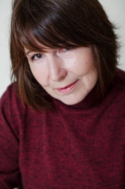 Yakın çekim parlak bir tek sesli arka plan üzerinde rötuş olmadan bir kadın portresi. Bordo kazaklı fram bakarak gülümseyen yaşlı güzel kadın