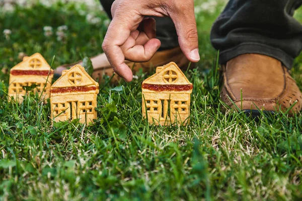 fabulous sweet house. Three cookies in the form of a house stand on a green meadow close-up. The hand of man puts one hous