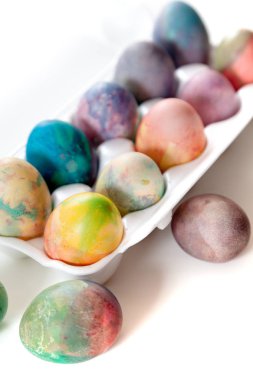 Paskalya tatiline özen göster. Farklı renklerde boyanmış birkaç tavuk yumurtası hücreli plastik bir kapta bulunur. Yakınlarda üç yumurta var.