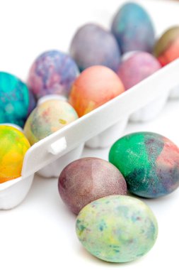 Paskalya tatiline özen göster. Farklı renklerde boyanmış birkaç tavuk yumurtası hücreli plastik bir kapta bulunur. Yakınlarda üç yumurta var.