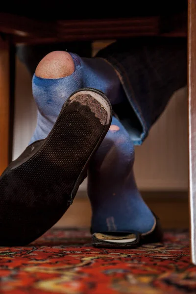 Man sits on chair on his socks can see holes