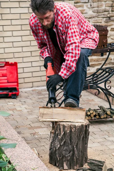 Man in plaid shirt is sawing  log on stumpт  electric saw — Stock Photo, Image