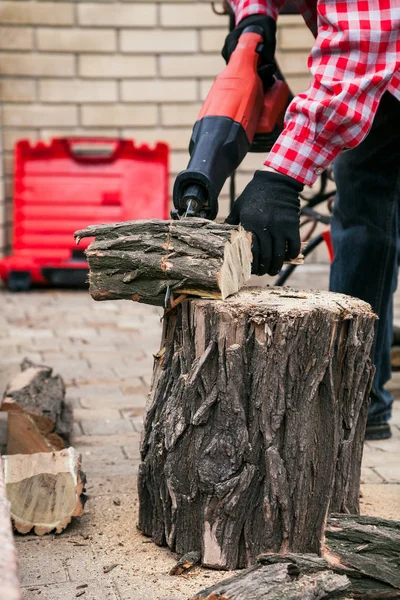 Man in plaid shirt is sawing log with electric saw — Stock Photo, Image