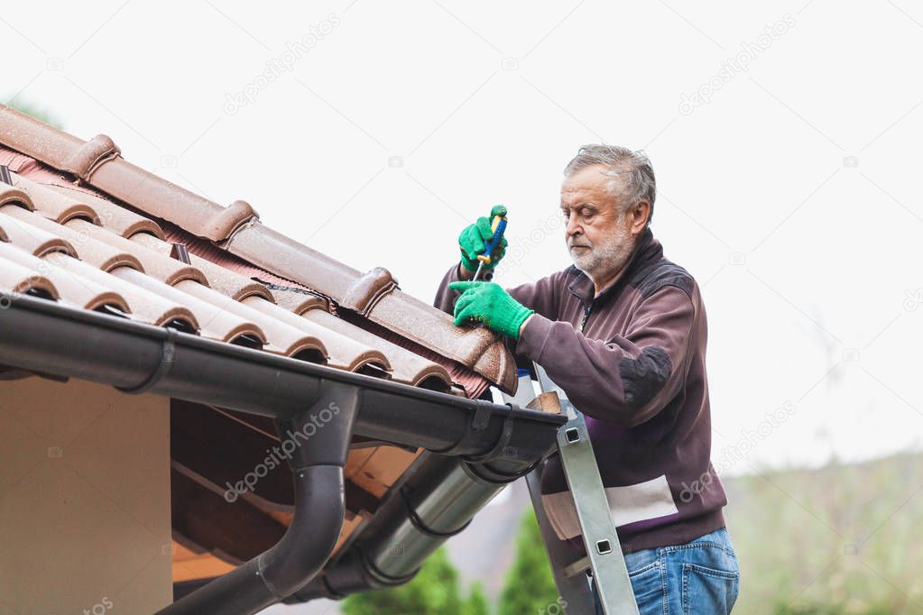 Man repairs a tiled roof of house close up