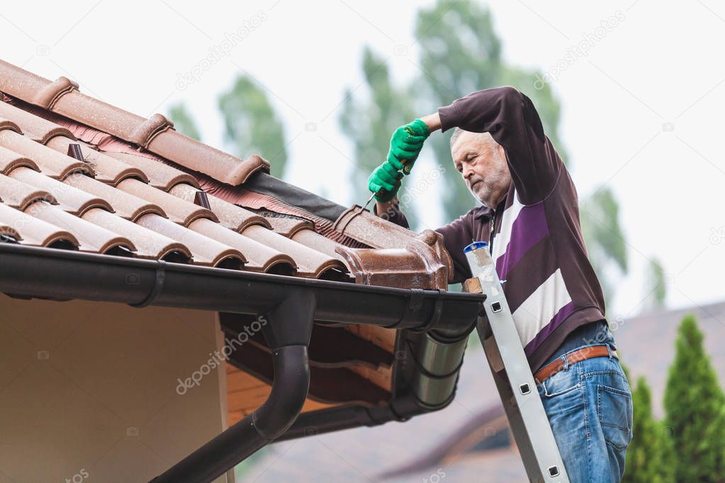 Man repairs a tiled roof of house close up