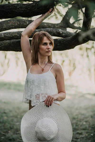 Cantik pirang memegang topi di depan pohon — Stok Foto