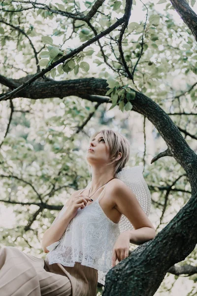 Linda rubia se sienta en el árbol — Foto de Stock