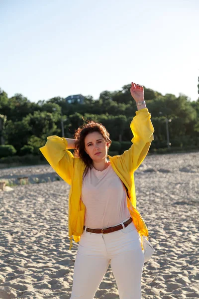 Krásná a veliká žena ve žlutém kabátku na písečné pláži — Stock fotografie