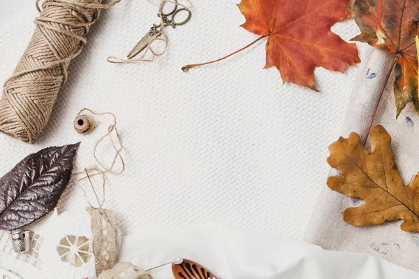 Tijeras, hilo y hojas caídas yacen sobre tela blanca —  Fotos de Stock