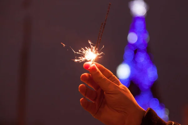 Bengala fogo no homem mãos na árvore de Natal luzes fundo — Fotografia de Stock