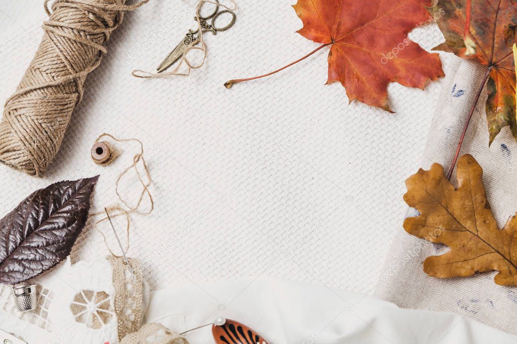 Scissors, thread and fallen leaves lie on white cloth