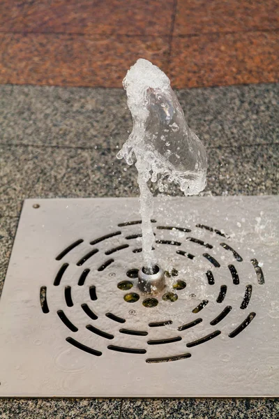 Jet of water from dry fountain beats out under granite slab.