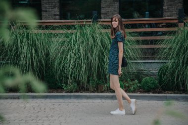 Yeşil elbiseli ince uzun kız cadde boyunca yürüyor