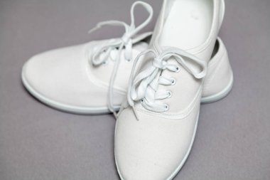 Gri arka planda duran beyaz spor ayakkabıları çifti