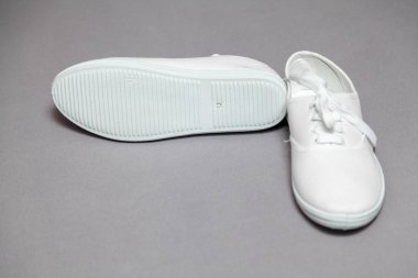 Gri arka planda duran beyaz spor ayakkabıları çifti