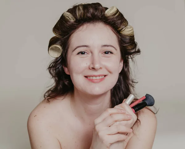 Ragazza con bigodini per capelli in possesso di cosmetici primo piano — Foto Stock