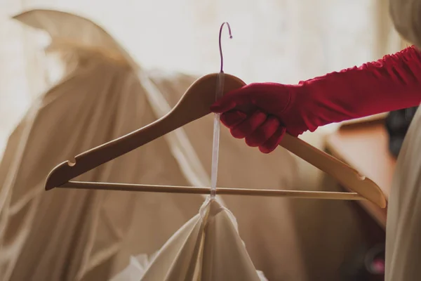 A mão na luva vermelha mantém o cabide com o vestido da noiva — Fotografia de Stock