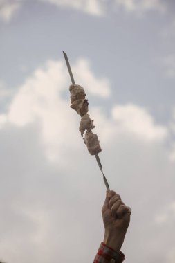 El gökyüzü arka planda et parçaları ile şiş tutar
