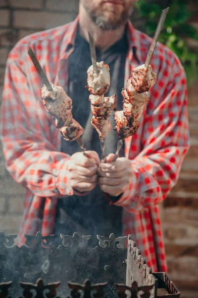 Человек с бородой держит три шашлыка с кусочками мяса — стоковое фото
