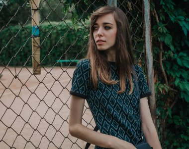 Genç ince kız tenis kortu önünde duruyor. 