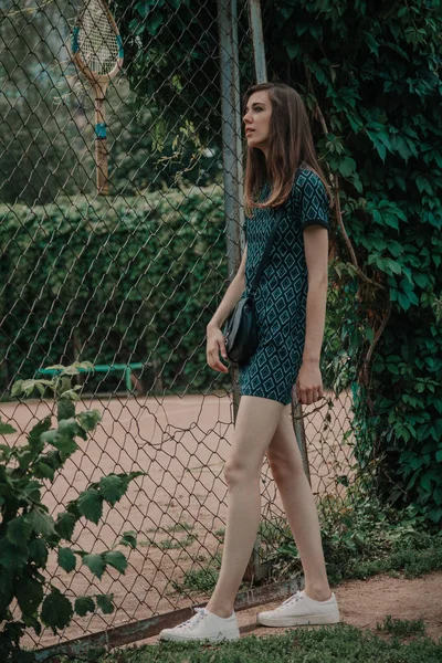 Young slim girl stands in front of  tennis court — Stock Photo, Image