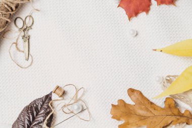 Makas, iplik ve düşmüş yaprakları beyaz bez üzerinde yatıyor