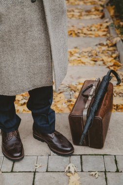 Man paltolu adam sonbahar parkında duruyor. Halı torbasının yanında