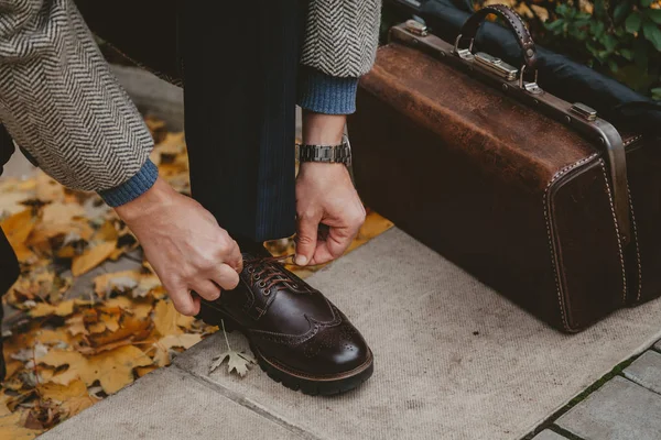 Beyefendi kahverengi ayakkabıya dantel bağlıyor. Yakında halı çantası var.