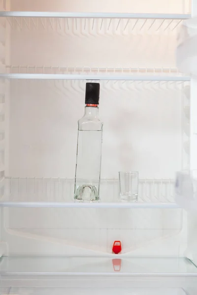 Botella de vodka y vidrio está en nevera vacía —  Fotos de Stock
