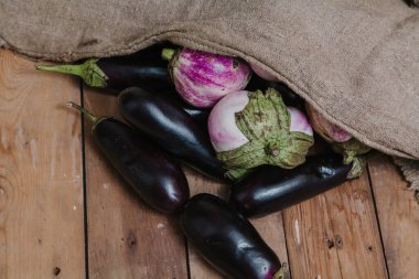 Mavi ve beyaz patlıcan tahtalarda yatıyor. Çantanın yanında