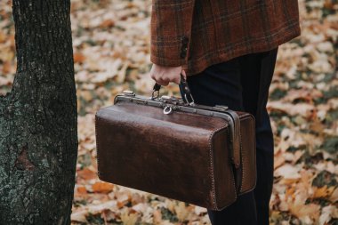 Ceketli adam elinde deri bavul tutuyor.