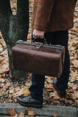 Ceketli adam elinde deri bavul tutuyor.