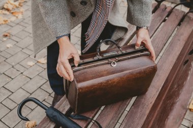 Eller ahşap bankta deri halı çantasını açar.