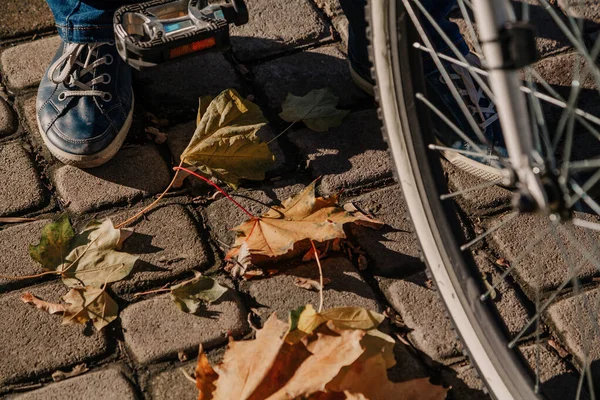 Stopa w tenisówkach stoi na jesiennym chodniku. Niedaleko rower — Zdjęcie stockowe