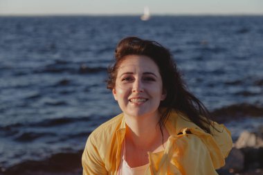 Uzun kızıl saçlı hoş bir kız su yüzeyinin arka planında duruyor. Doğal kusurlarıyla rötuş yapmayan bir kadının portresi