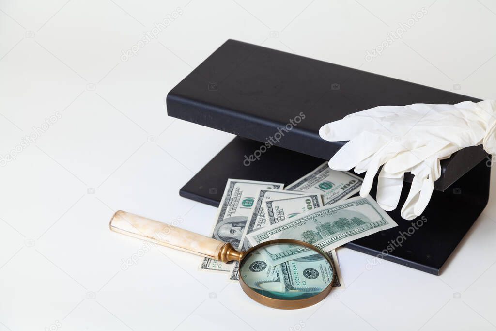 Verification of dollar bills using a close-up UV detector. Nearby lies a magnifying glass on a bone handle and rubber glove