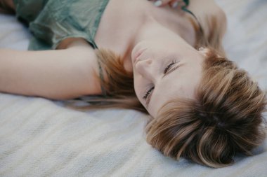 Genç ve çekici bir kadın ince zeytin rengi bir bluzla beyaz bir ekose üzerinde yatıyor. Ters portre.