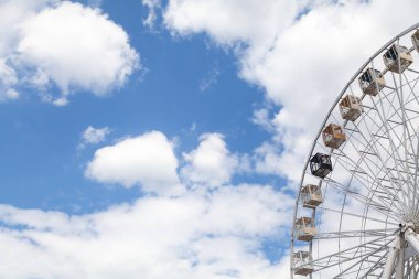 Çekiciliğe bakıyorum. Dönme dolapta beyaz bulutlu mavi gökyüzüne karşı kulübeler.