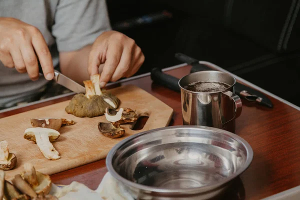 Toplanan mantarların incelenmesi. Tahta bir yaban domuzunun üstünde yenebilir mantar kesen bir adamın elleri.