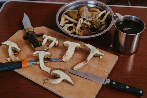 Mantar hala hayat. Kesme tahtasının üzerinde çiğ mantar ve üç bıçak var. Metal dishe yakınlarında.