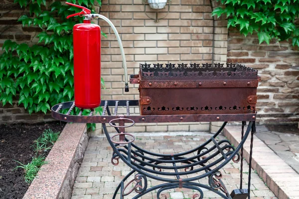 Μπάρμπεκιου Και Πυροσβεστήρας Ένας Μεγάλος Κόκκινος Πυροσβεστήρας Στέκεται Ένα Σφυρηλατημένο — Φωτογραφία Αρχείου