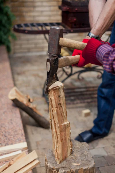 Strong log. Four hands in red gloves chop a round log with an ax and a sledgehammer on a stump in a summer yar