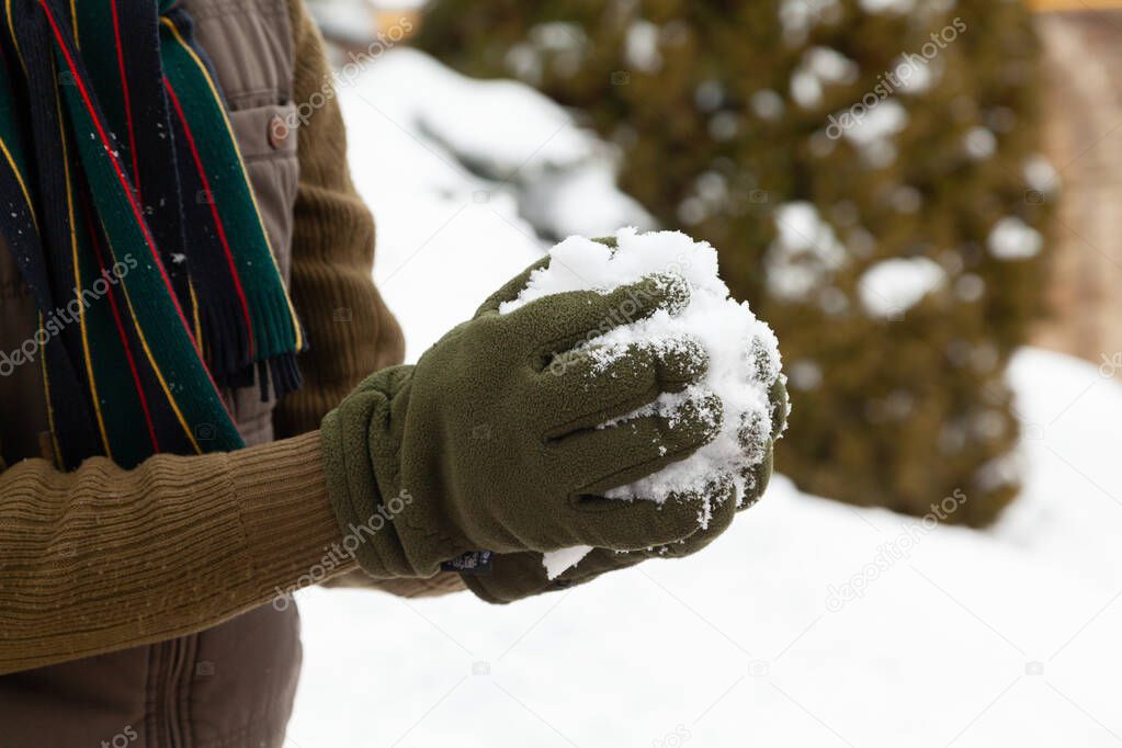 Winter fun. Hands in green fleece gloves form snowballs on a frosty day close-u