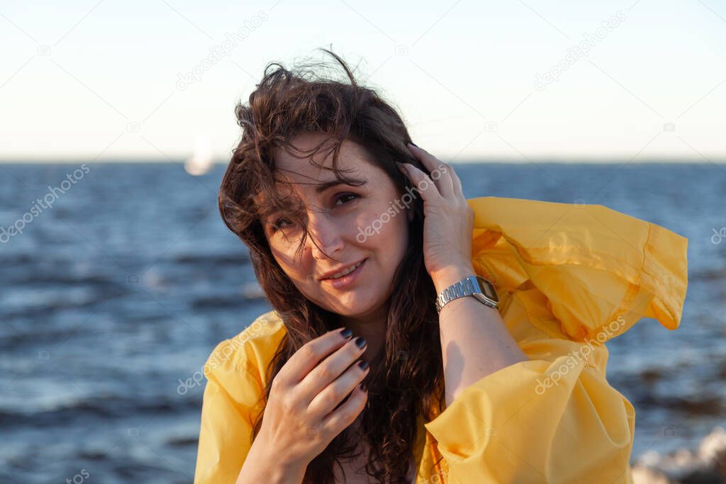 Nice girl with long red hair is standing on the background of a water surface. Portrait of a woman without retouching with her natural imperfection