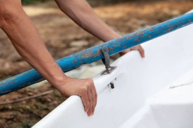 Balıkçı elleri beyaz teknenin yanında dinleniyor. Tahta kürek ingiliz anahtarının üzerinde duruyor.