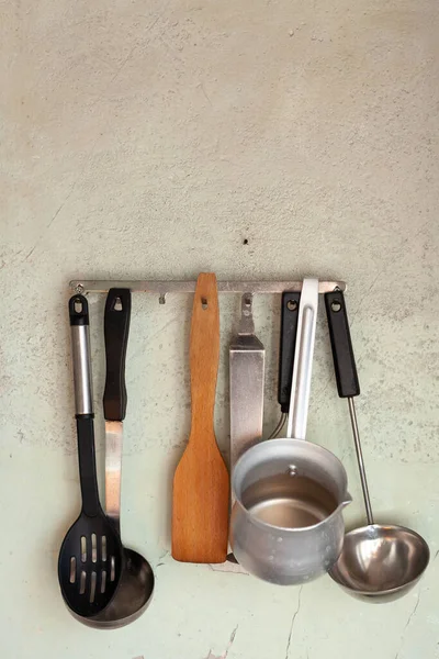 vintage set of kitchen fixtures hangs on an empty wall. A wooden spatula weighs between the metal tool