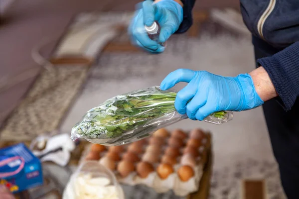 Prevention of infection. A hand in a blue rubber glove sprays an aerosol antiseptic on a bunch of green herbs in a package. Close-up