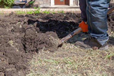 Kot pantolonlu bir adam kürekle toprağı kazıyor. Kuru otlar homurdanıyor