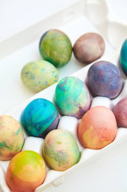 Paskalya tatiline özen göster. Farklı renklerde boyanmış birkaç tavuk yumurtası hücreli plastik bir kapta bulunur. Yakınlarda üç yumurta var.